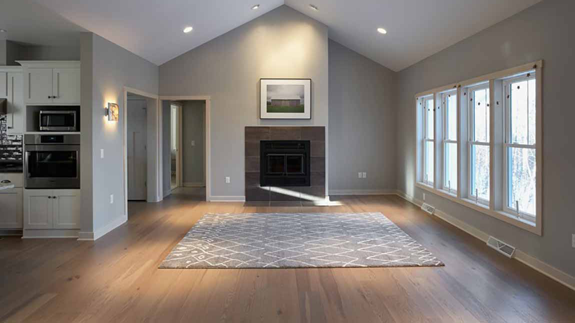 An empty living room with a fire place, area rug, and hardwood flooring